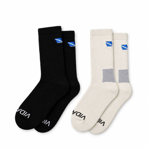 Two pairs of crew socks on a white background: one pair is black with a small blue logo near the cuff and black text near the toe, and the other pair is off-white/cream with a gray block at the ankle and a small blue logo near the cuff. The word 'VIDA' is visible on the socks.