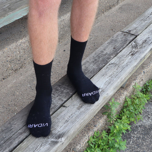 Black toe socks with white 'VIDA&R' branding worn on a person's feet while standing on weathered wooden steps outdoors.